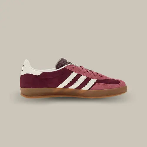 La Adidas Gazelle Indoor Maroon Preloved Crimson vue de côté avec sa base de couleur bordeaux avec des superpositions en dail rose. On retrouve les trois bandes blanches accordés au heel tab.