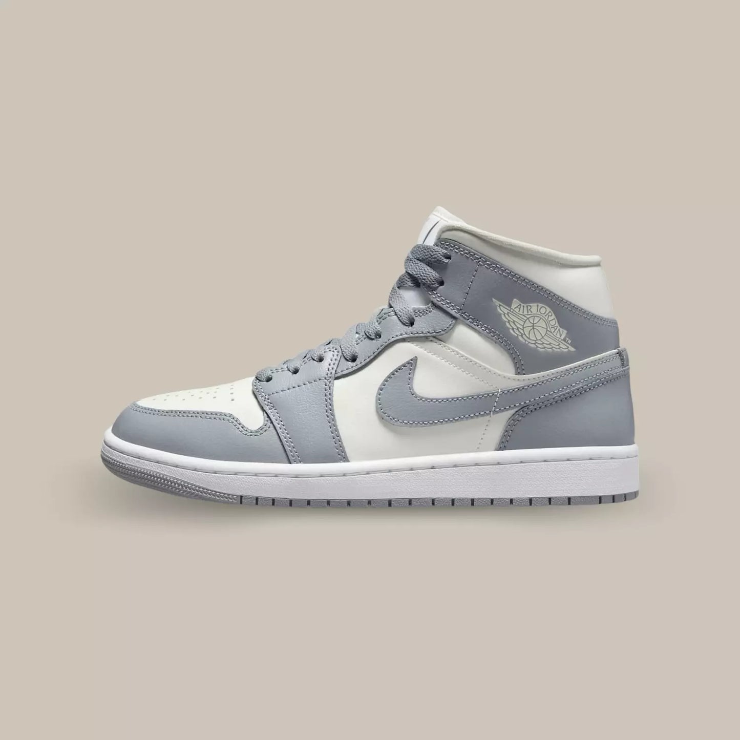 La Air Jordan 1 Mid Grey Sail de coté avec sa base en cuir blanc et ses superpositions en cuir gris.