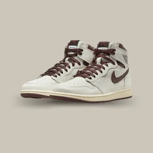 La Air Jordan 1 Retro High OG A Ma Maniére possède une base en cuir suédé blanc cassé avec des empiècements au motif snakeskin comprenant des rappels de couleurs oscillant entre le bordeaux et le marron. Une midsole crème vient renforcer le côté vintage de la paire.
