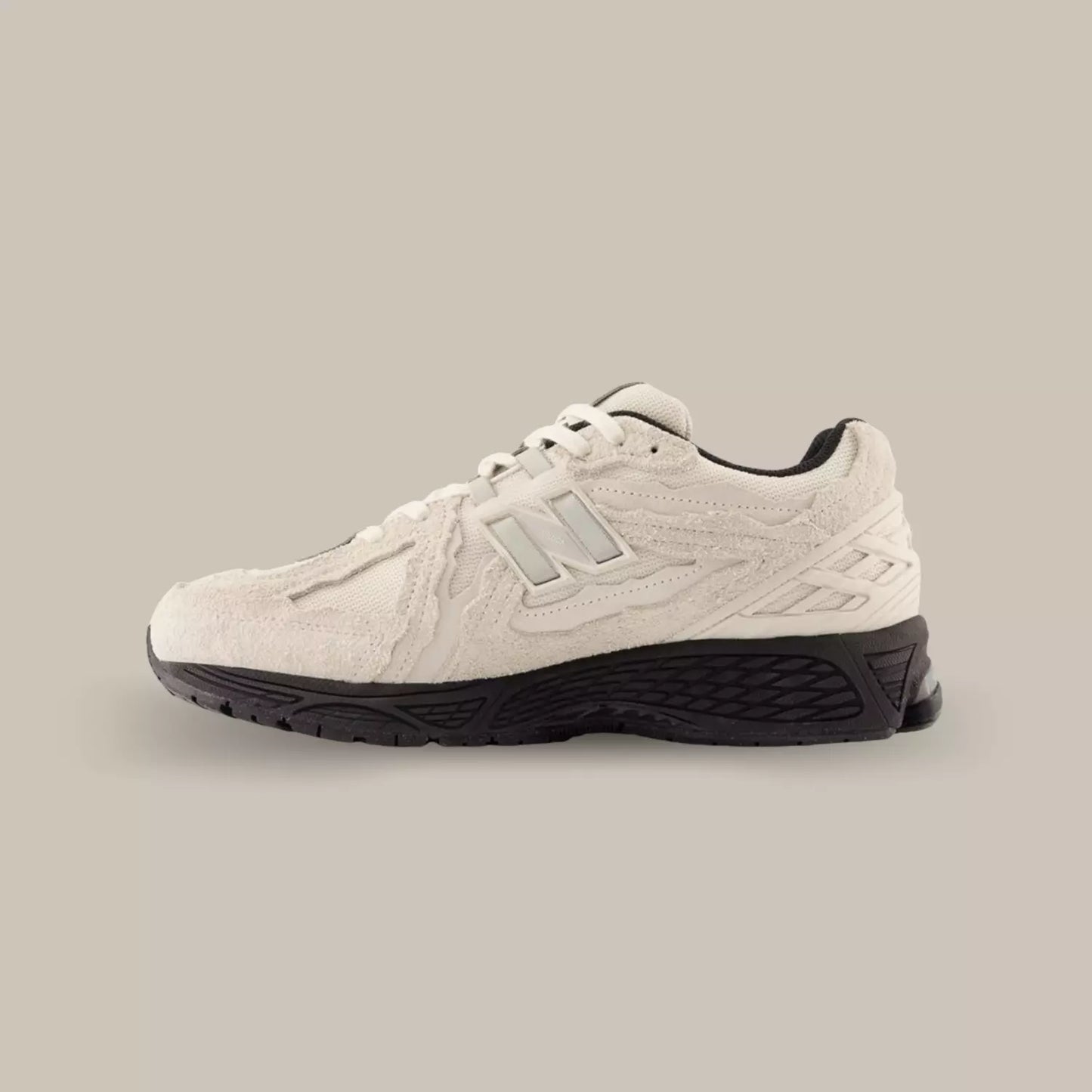 La New Balance 1906R Protection Pack Beige de coté avec une base en mesh beige accompagnée d’empiècements en suède et hairy suède ton-sur-ton dans un style déstructuré.