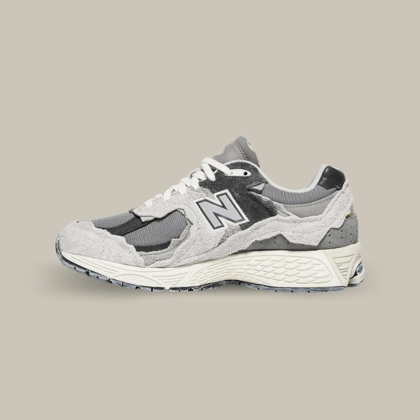 La New Balance 2002R Protection Pack Rain Cloud de coté avec sa base en mesh de couleur gris, noir et des touches subtiles de bleu. On retrouve des superpositions en suède de couleur grise.