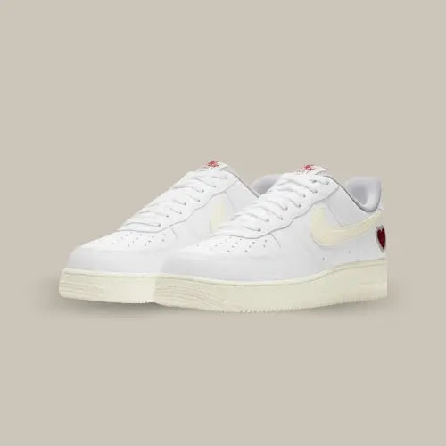 La Nike Air Force 1 Low Valentine's Day (2021) possède une base en cuir blanc avec des rappels de couleurs crème au niveau du swoosh et de la midsole. On retrouve un coeur rouge posé sur le talon et l'inscription "NIKE AIR" sur la languette et le talon.