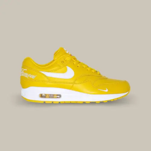 La Nike Air Max 1 '87 SP Supreme Speed Yellow vue de côté avec sa base en cuir jaune et son swoosh blanc accordé aux écritures "World Famous" sur le talon, à la midsole et au mini-swoosh à l'avant de la chaussure.