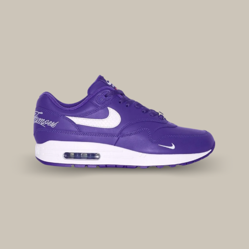 La Nike Air Max 1 '87 SP Supreme Varsity Purple vue de côté avec sa base en cuir violet et son swoosh blanc accordée au écritures sur le talon "World Famous" et la midsole ainsi que le mini swoosh à l'avant de la chaussure.