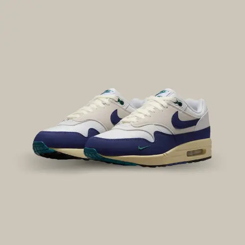 Nike Air Max 1 Athletic Department Deep Royal Blue vue de trois quarts, sneaker en mesh blanc et cuir bleu royal avec semelle crème et unité Air visible, design rétro et détails verts contrastants.