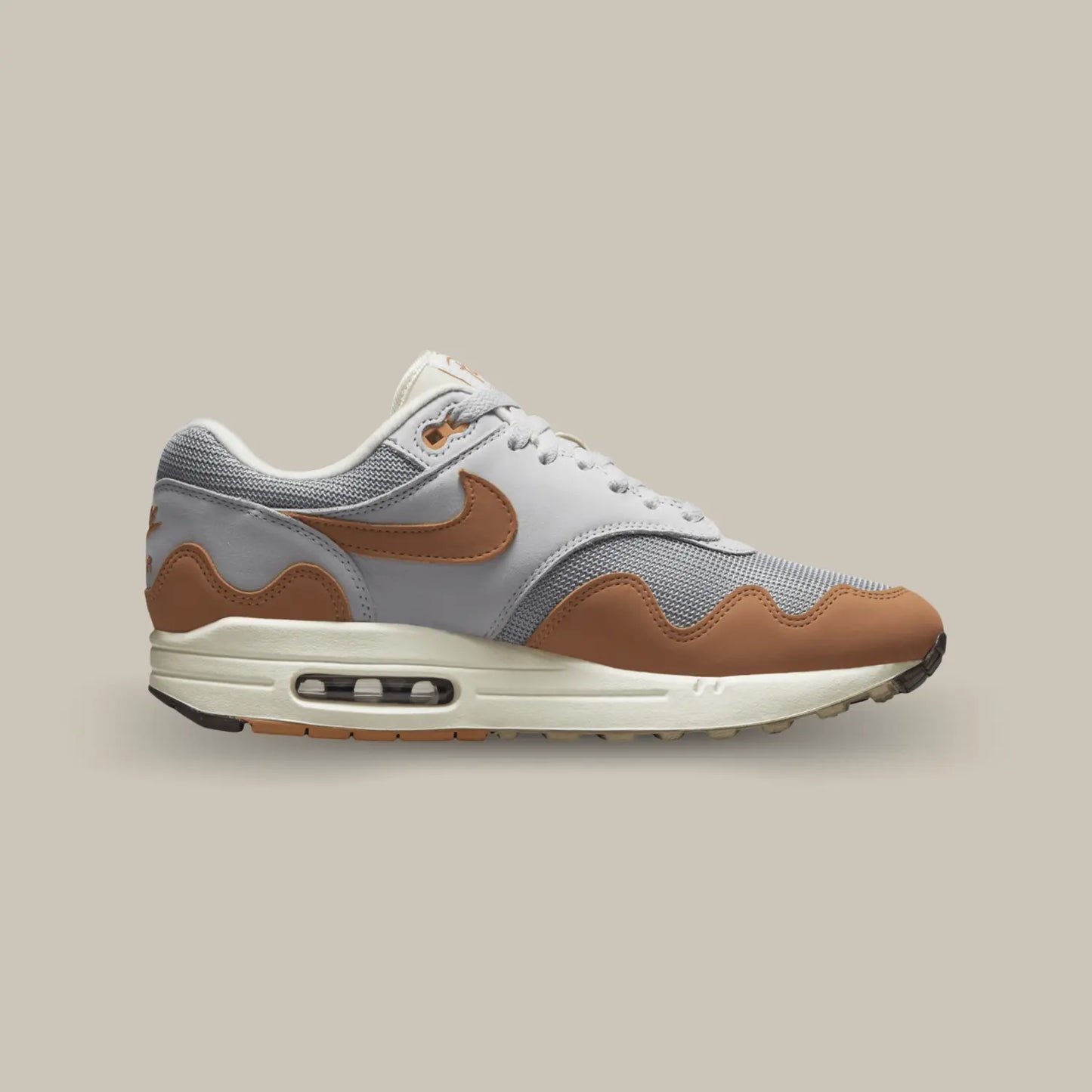 La Nike Air Max 1 Patta « Monarch » de coté avec sa base en mesh gris, couplée à des empiècements en cuir blanc, on retrouve également un swoosh de couleur orange accompagnant les vagues au dessus de la midsole.