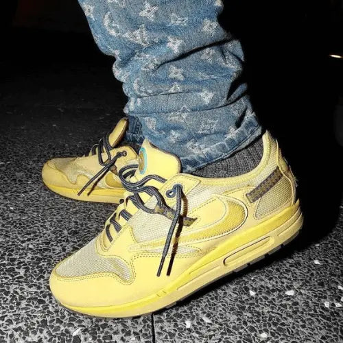 La Nike Air Max 1 Travis Scott Cactus Jack Saturn Gold portée avec jean bleu clair portant les motifs Louis Vuitton.