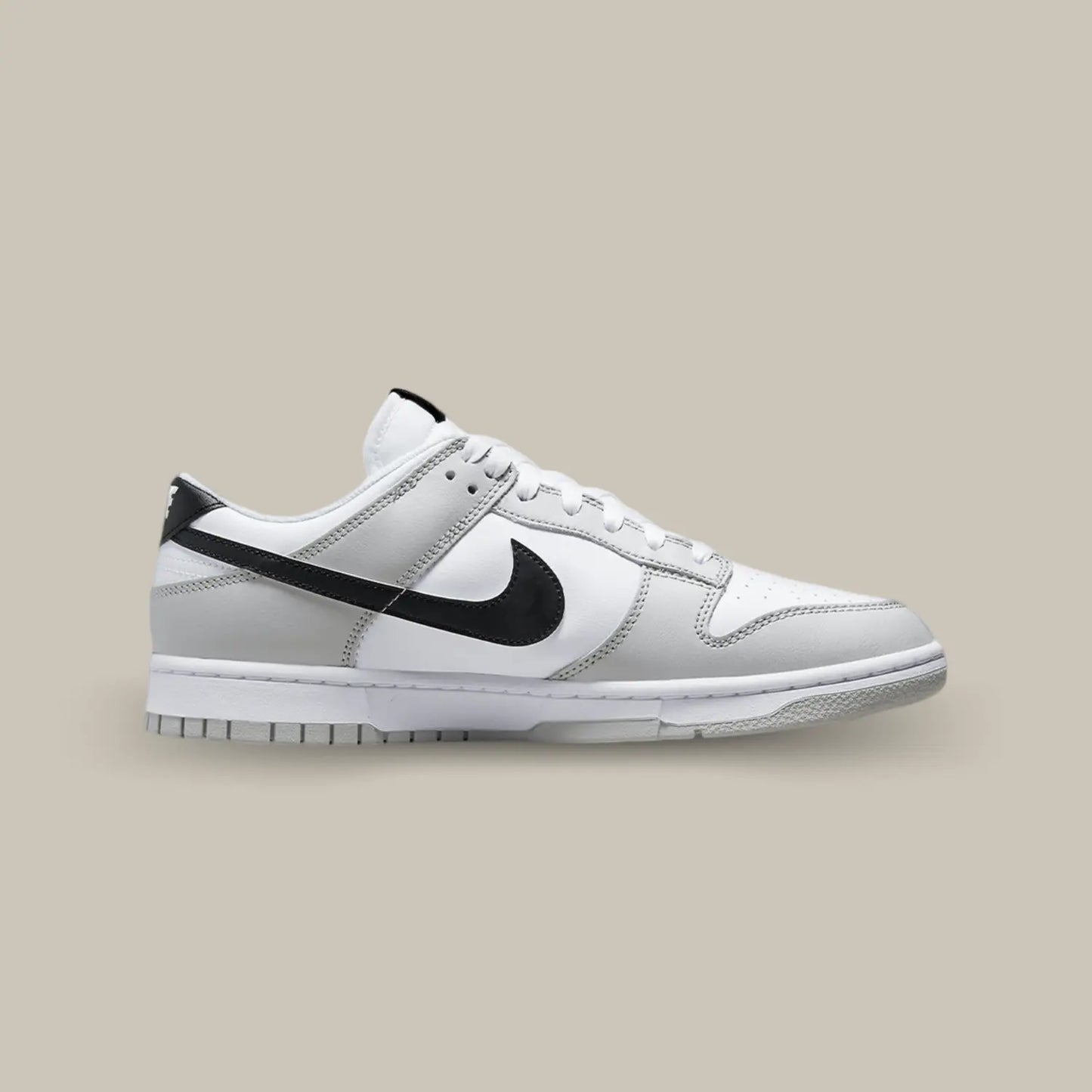 La Nike Dunk Low Lottery Pick Grey Fog de coté avec sa base en cuir blanc accompagné de superpositions en cuir gris. On retrouve des swooshes noirs que l’on peut gratter, avec le hangtag fourni, pour laisser apparaitre des motifs rouges.