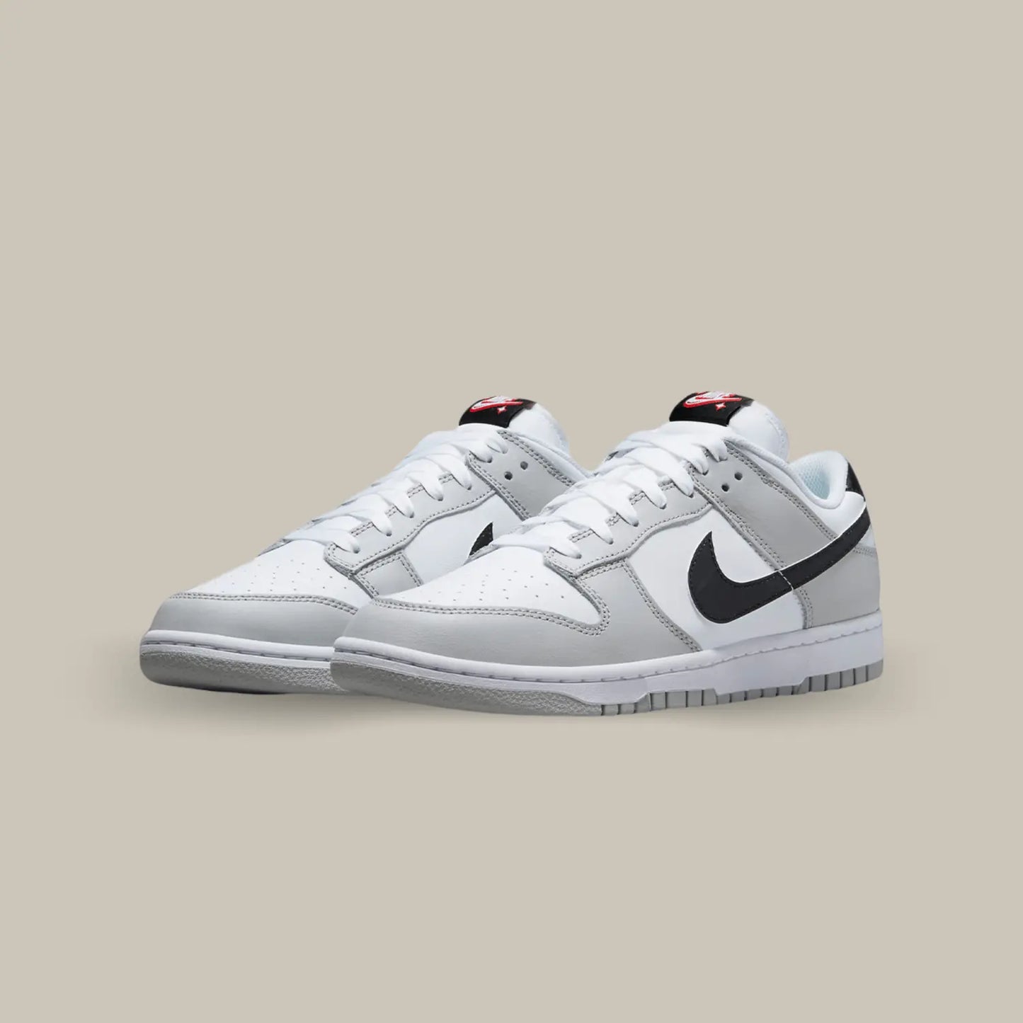 La Nike Dunk Low Lottery Pick Grey Fog présente une base en cuir blanc accompagné de superpositions en cuir gris. On retrouve des swooshes noirs que l’on peut gratter, avec le hangtag fourni, pour laisser apparaitre des motifs rouges.