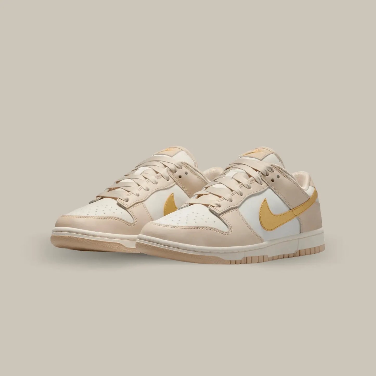 La Nike Dunk Low Phantom Metallic Gold affiche une base en cuir blanc cassé accompagnée de superpositions en cuir à mi-chemin entre le beige et le rose pâle.
