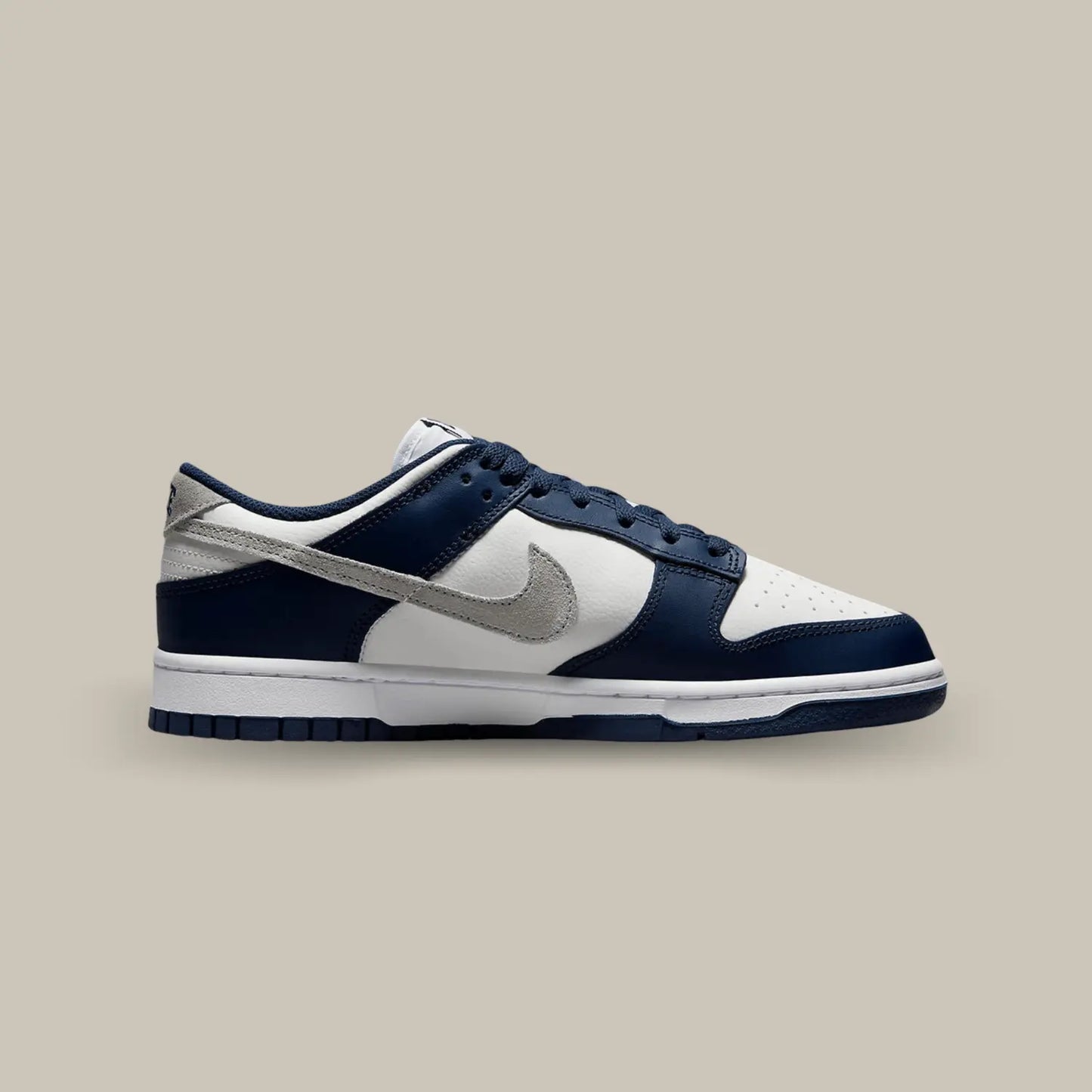 La Nike Dunk Low Summit White Midnight Navy de coté avec une base en cuir grainé blanc cassé aux superpositions de cuir bleu marine.