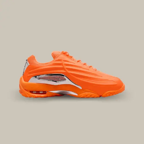 La Nike Hot Step 2 NOCTA Total Orange de côté avec son coloris orange et ses ondulations au dessus d'une plaque réfléchissante donnant un aspect futuriste à la paire.