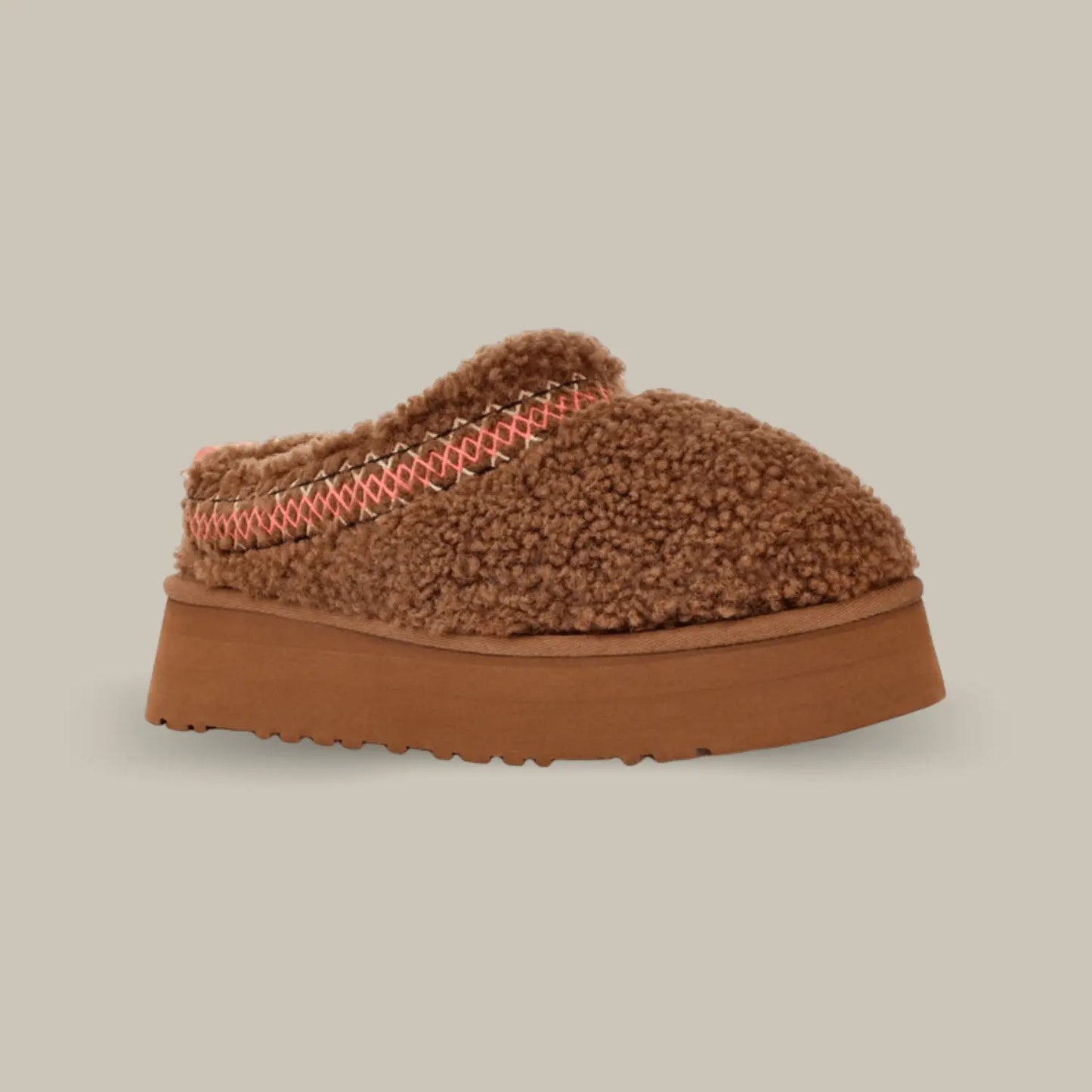 La UGG Tazz Braid Hardwood de coté avec sa tige en duvet marron, son épaisse tresse rouge et noir en polyester recyclé et sa semelle compensée de 4.4cm en EVA.