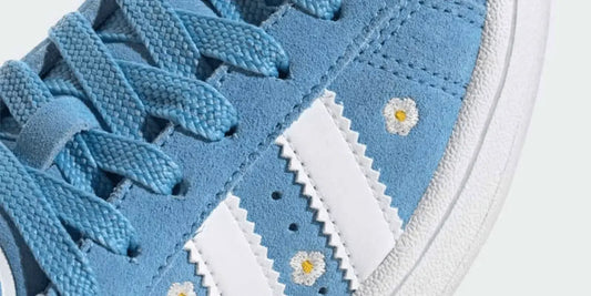 Une Adidas Campus bleu avec des petites fleurs parsemées sur la chaussure.