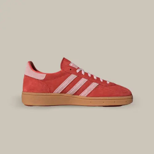 La Adidas Handball Spezial Bright Red Clear Pink vue de coté avec son coloris rouge, ses trois bande roses pale accordé au heel tab. Le logo Spezial est de couleur or et on retrouve la semelle en gomme.