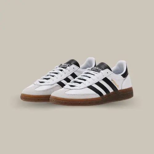 La<strong> Adidas Handball Spezial White Black Gum</strong> possède une base en <strong>cuir blanc</strong> avec les trois célèbres bandes en <strong>cuir noir</strong> accordée au heel tab et à la languette. On retrouve un mudguard en <strong>daim gris</strong> et l'inamovible semelle en gomme.