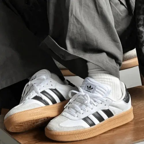 La Adidas Samba XLG White Black Gum porté avec un pantalon large gris foncé.