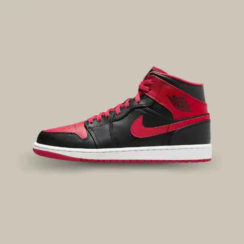La Air Jordan 1 Mid Alternate Bred (2022) vue de côté avec son cuir noir et ses empiècements rouges au niveau de la toebox, du swoosh et des rabats.