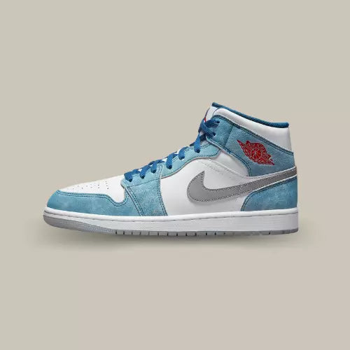 La Air Jordan 1 Mid French Blue Fire Red de coté avec sa base en cuir blanc et ses empiècements en suède bleu clair.