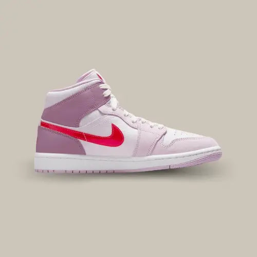 La Air Jordan 1 Mid Valentine's Day (2022) de côté avec sa base en cuir blanc, ses tons roses et son swoosh rouge accordé au logo Jordan.
