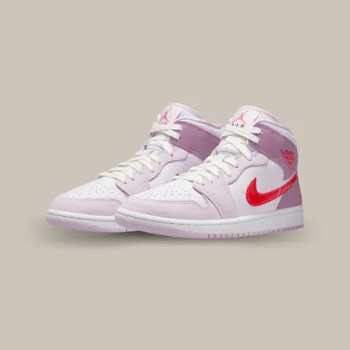 La Air Jordan 1 Mid Valentine's Day (2022) possède une base en cuir blanc avec des superpositions en cuir rose claire. On retrouve du cuir mauve sur l'ensemble du talon qui contraste avec le rouge du logo Jordan et du swoosh. Ce trio de roses est parfait pour plaire aux amoureux.