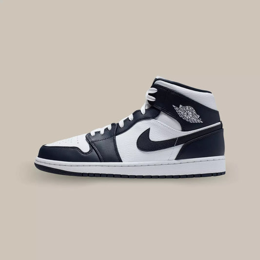 La Air Jordan 1 Mid White Metallic Gold Obsidian de coté avec sa base en cuir blanc sublimée par des superpositions en cuir d’un bleu très foncé, presque noir.