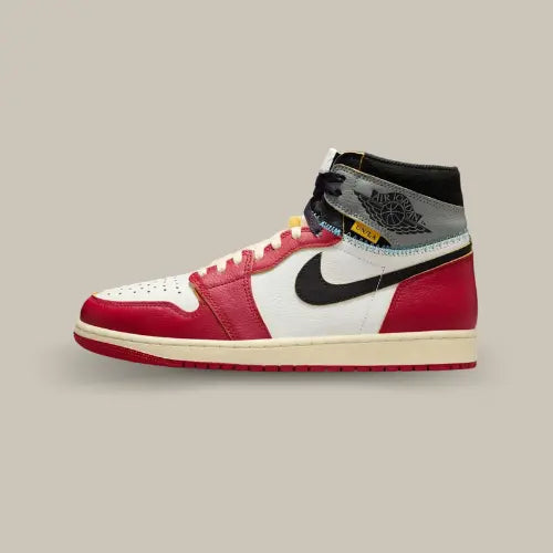 La Air Jordan 1 Retro High OG SP Union LA Chicago Shadow vue de côté avec sa base en cuir blanc blanc et ses empiècement rouge. On retrouve un swoosh noir et un empiècement gris comportant le logo Air Jordan noir au niveau de la cheville avec la petite étiquette jaune représentatif de Union.