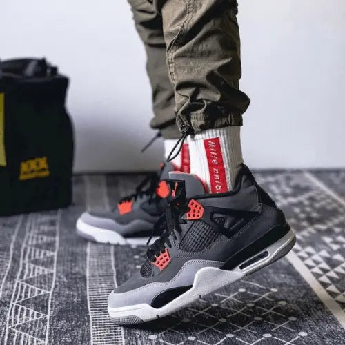 La Air Jordan 4 Infrared (2022) portée avec des chaussettes blanches et un logo rouge.