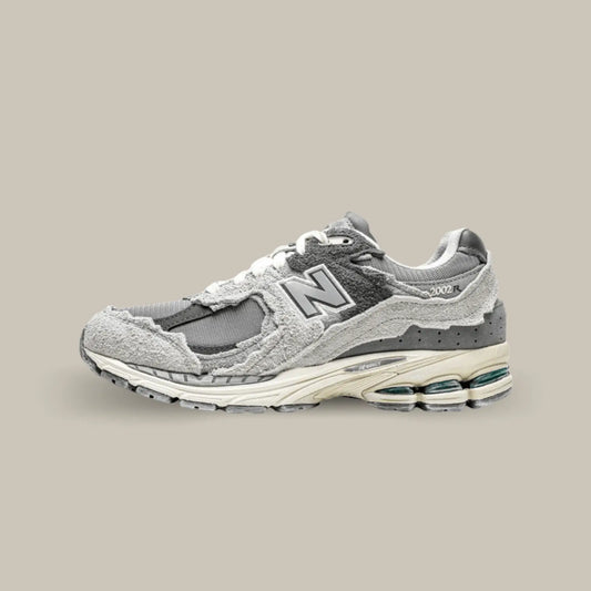 La New Balance 2002R Protection Pack Rain Cloud de coté avec sa base en mesh de couleur gris, noir et des touches subtiles de bleu. On retrouve des superpositions en suède de couleur grise.