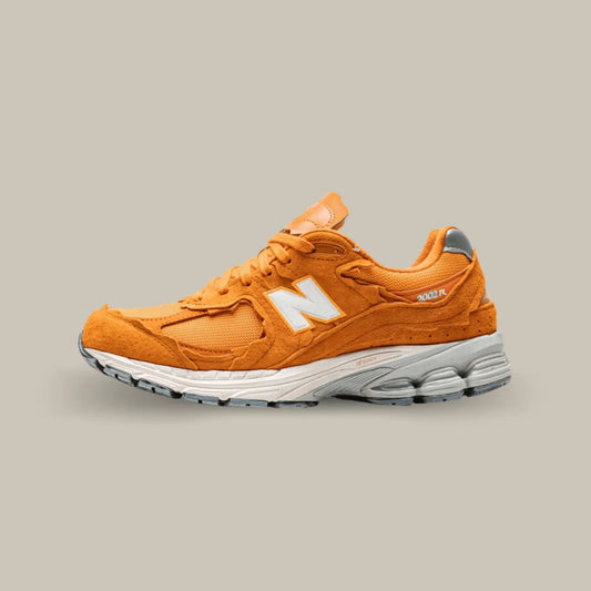 La New Balance 2002R Protection Pack Vintage Orange de coté avec sa base en mesh dans son aspect déconstruit et son suède orange sur les superpositions.