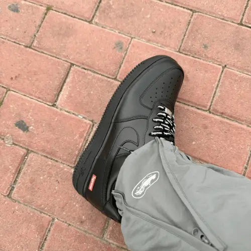 La Nike Air Force 1 Supreme Black portée avec un pantalon gris Cortez.
