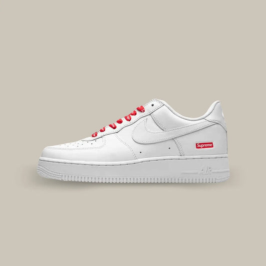 La  Nike Air Force 1 White Supreme de coté avec son classique cuir blanc et la petite touche Supreme avec le logo sur fond rouge.