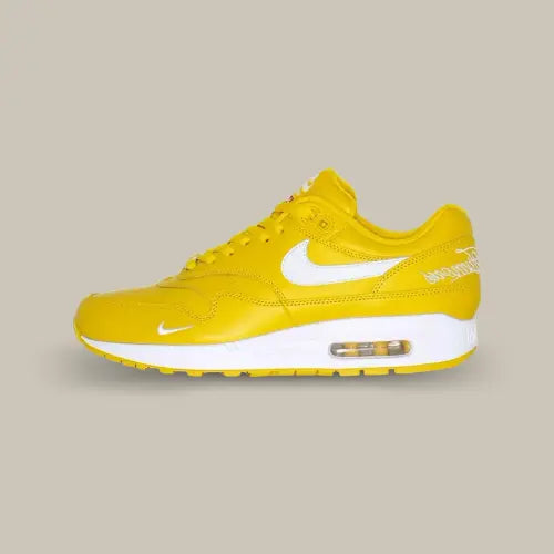La Nike Air Max 1 '87 SP Supreme Speed Yellow vue de côté avec sa base en cuir jaune et son swoosh blanc accordé aux écritures "World Famous" sur le talon, à la midsole et au mini-swoosh à l'avant de la chaussure.