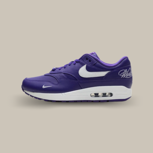 La Nike Air Max 1 '87 SP Supreme Varsity Purple vue de côté avec sa base en cuir violet et son swoosh blanc accordée au écritures sur le talon "World Famous" et la midsole ainsi que le mini swoosh à l'avant de la chaussure.