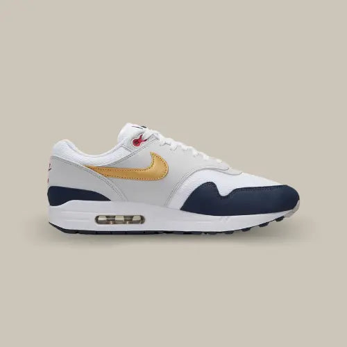 Nike Air Max 1 Olympic vue latérale intérieure, sneaker blanche avec détails bleu marine, Swoosh doré et œillets rouges, silhouette rétro emblématique avec unité Air visible.
