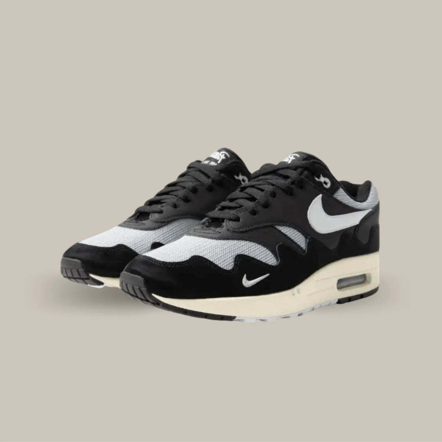 La Nike Air Max 1 Patta Black Grey possède une base en mesh gris avec des superpositions en cuir noir. On retrouve les vagues dans un effet élégant qui est la signature de la collection. Les détails blanc comme le « Nike Air » au talon, le swoosh brodé viennent donné de l’éclat à la paire.