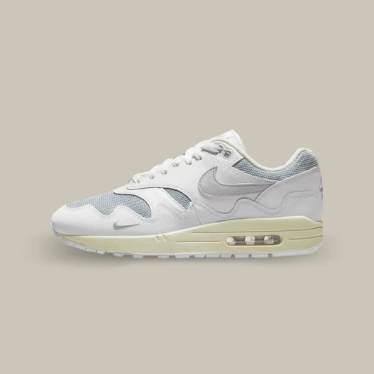 La Nike Air Max 1 Patta White Grey de coté avec une base en mesh gris complétée par des superpositions de cuir blanc.