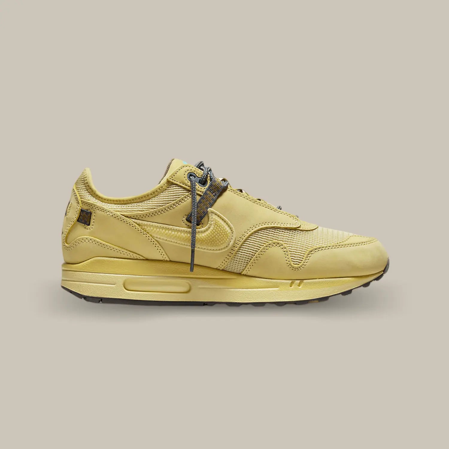 La Nike Air Max 1 Travis Scott Cactus Jack Saturn Gold de coté avec une base en mesh jaune « Wheat » et différents empiècements de la même couleur en daim. On retrouve le swoosh inversé qui a fait le succès de la collaboration entre Nike et Cactus Jack. On trouve un branding Cactus Jack sur le talon et la languette.