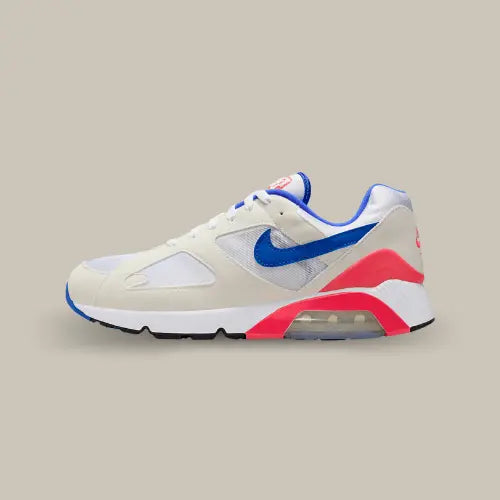 La Nike Air Max 180 Ultramarine (2024) vue de côté avec son coloris blanc cassé, son swoosh bleu et ses touches de rouge sur le talon et autour de l'unité Air visible à 180 degrés.