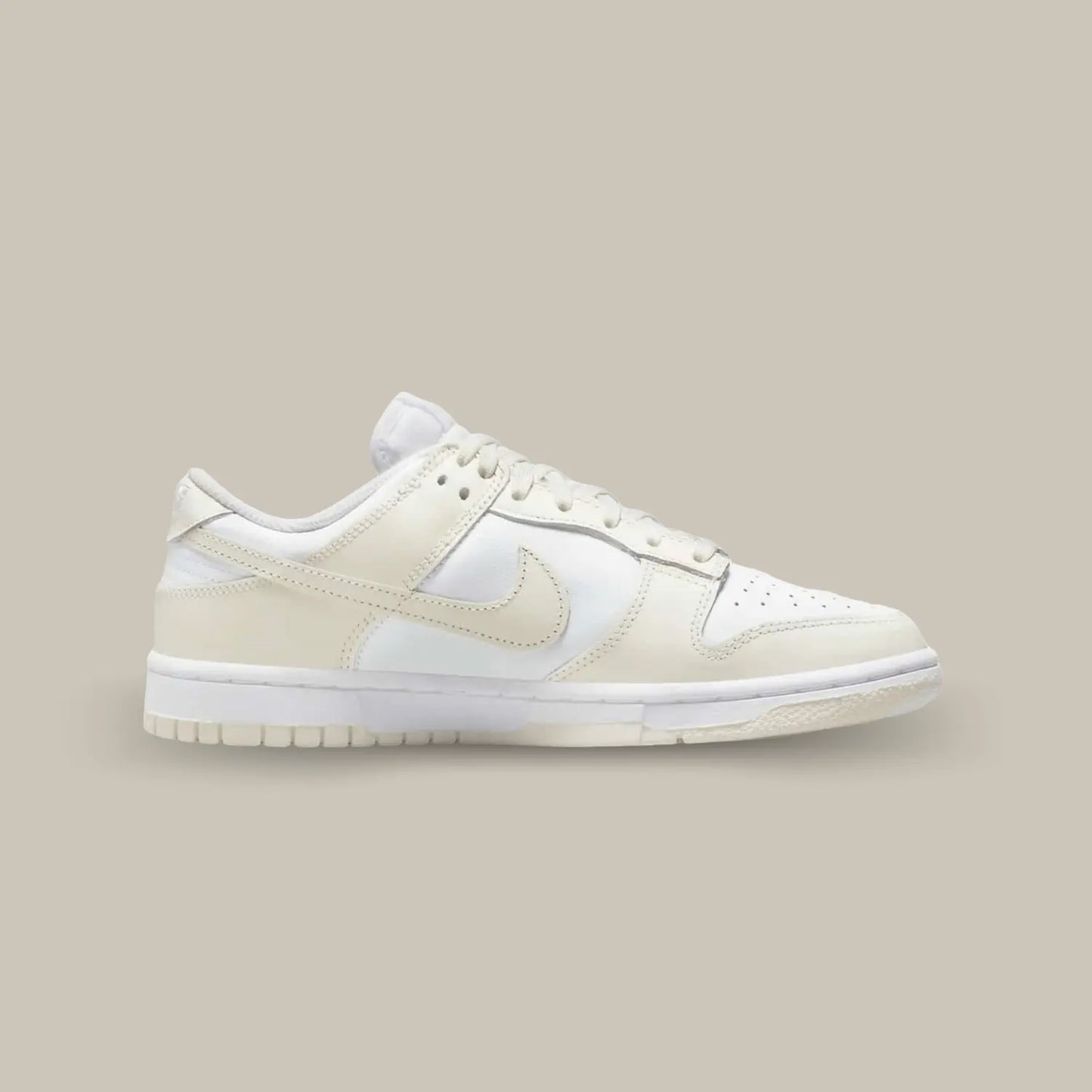 La Nike Dunk Low Coconut Milk de coté avec sa base en cuir blanc cassé, surélevée par des empiècements en cuir beige pastel.