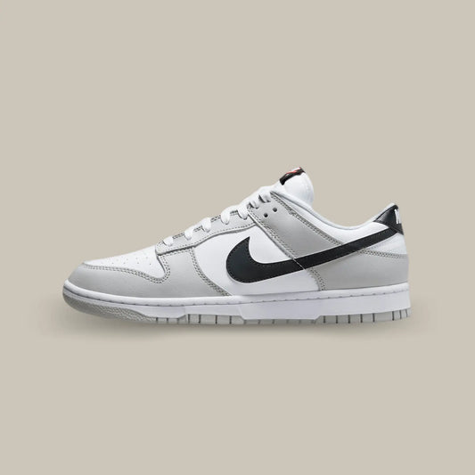 La Nike Dunk Low Lottery Pick Grey Fog de coté avec sa base en cuir blanc accompagné de superpositions en cuir gris. On retrouve des swooshes noirs que l’on peut gratter, avec le hangtag fourni, pour laisser apparaitre des motifs rouges.