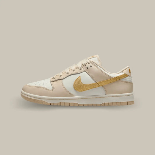 La Nike Dunk Low phantom Metallic Gold de coté avec sa base en cuir blanc et des superpositions en cuir à mi-chemin entre le beige et le rose pâle.