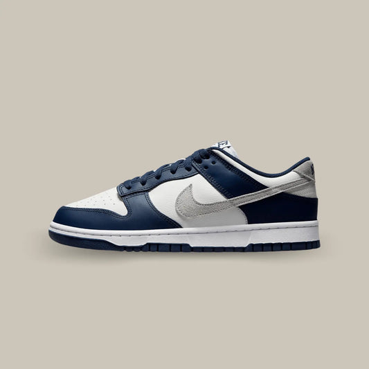 La Nike Dunk Low Summit White Midnight Navy  de coté avec une base en cuir grainé blanc cassé aux superpositions de cuir bleu marine.