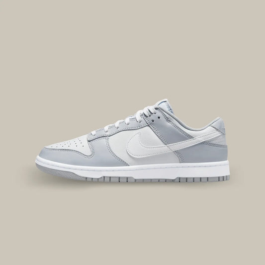 La Nike Dunk Low Two Tone Grey de coté avec sa base en cuir blanc, accompagnée par des superpositions en cuir gris sur les œillets, le mudguard et le talon.