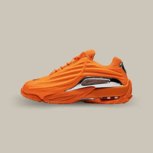 La Nike Hot Step 2 NOCTA Total Orange de côté avec son coloris orange et ses ondulations au dessus d'une plaque réfléchissante donnant un aspect futuriste à la paire.