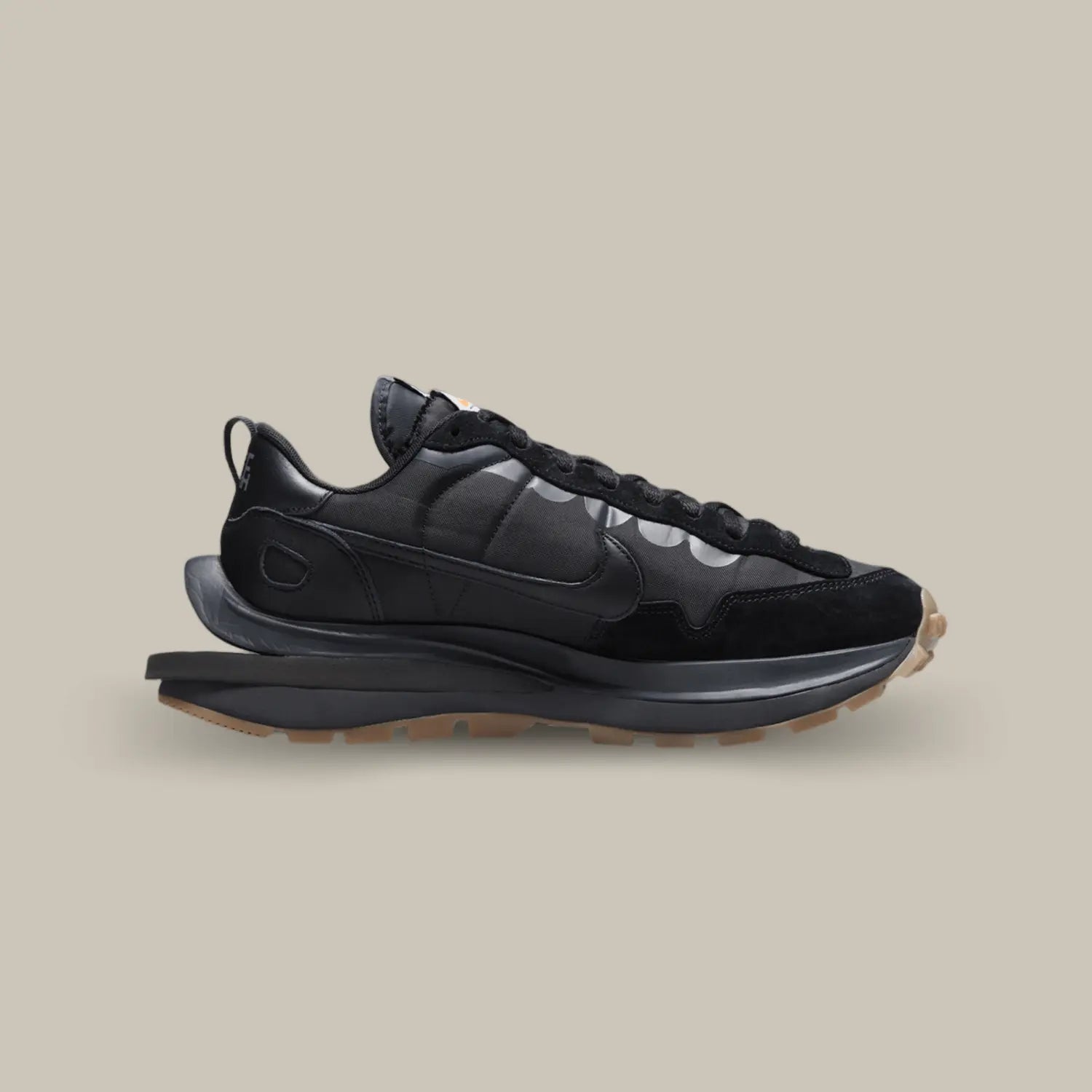 La Nike Vaporwaffle Sacai Black Gum de coté avec un design composé de superpositions de matières et d’éléments dédoublés. Elle se pare d’un upper en suède et tissu nylon, le même matériau que l’on a pu retrouver sur les LD Waffle Triple Black et White. Chacun des éléments est présenté en noir et s’accorde à la midsole. Pour créer un léger contraste, l’outsole opte quant à elle pour du gum.