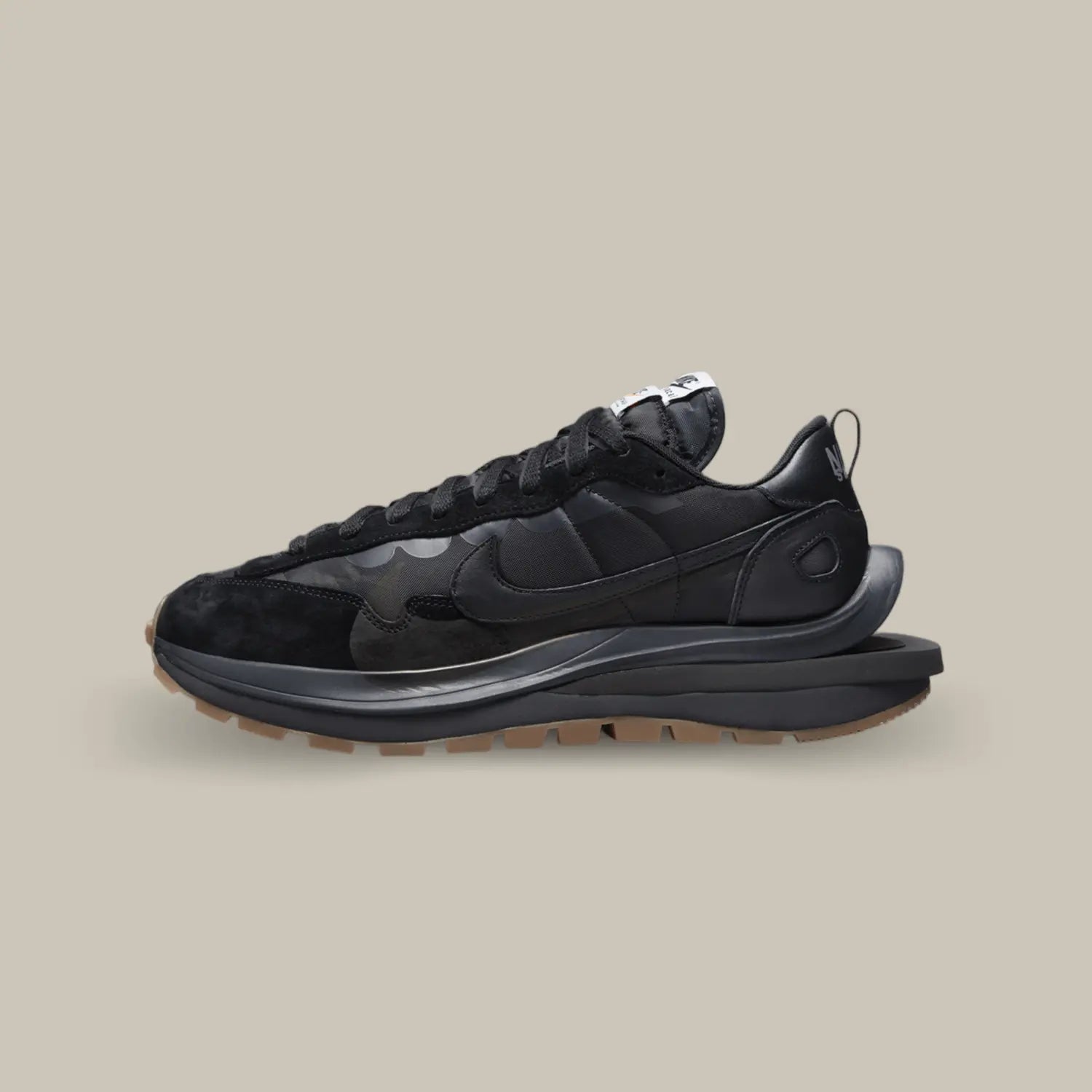 La Nike Vaporwaffle Sacai Black Gum de coté avec un design composé de superpositions de matières et d’éléments dédoublés. Elle se pare d’un upper en suède et tissu nylon, le même matériau que l’on a pu retrouver sur les LD Waffle Triple Black et White. Chacun des éléments est présenté en noir et s’accorde à la midsole. Pour créer un léger contraste, l’outsole opte quant à elle pour du gum.