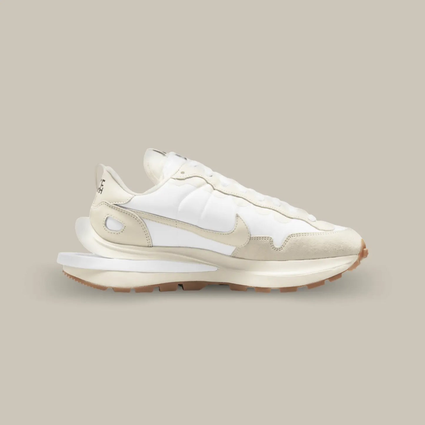 La Nike Vaporwaffle Sacai Sail Gum de coté avec un design composé de superpositions de matières et d’éléments dédoublés. Le upper joue sur une palette de couleurs très proches les unes des autres avec du blanc et blanc cassé, ce qui donne une allure élégante et sophistiquée à cette itération.