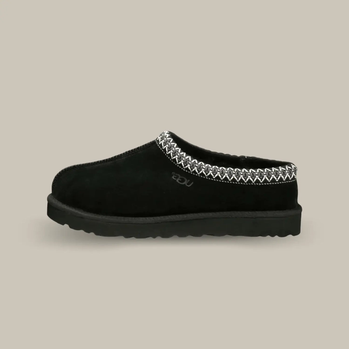 La Ugg Tasman Slipper Black de coté avec sa tige en daim noir, son tressage en polyester recyclé gris et blanc et sa semelle en EVA.