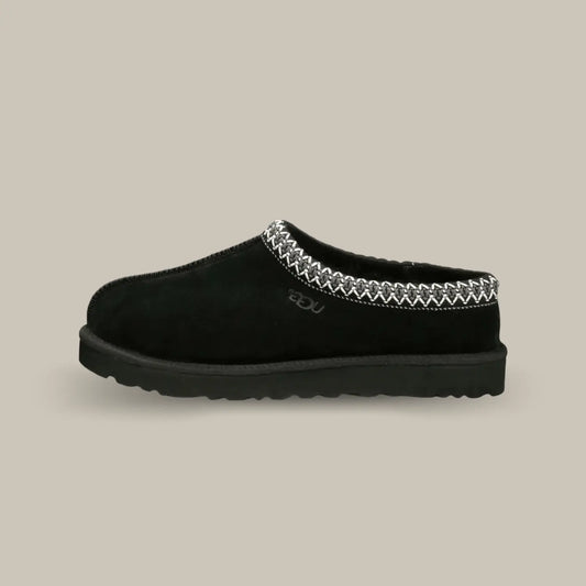 La Ugg Tasman Slipper Black de coté avec sa tige en daim noir, son tressage en polyester recyclé gris et blanc et sa semelle en EVA.